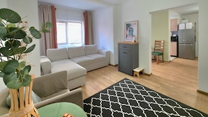 Ein Wohnzimmer mit einer Couch, einem kleinen Tisch, einer Pflanze und einer Küchenzeile mit Kühlschrank und Mikrowelle.