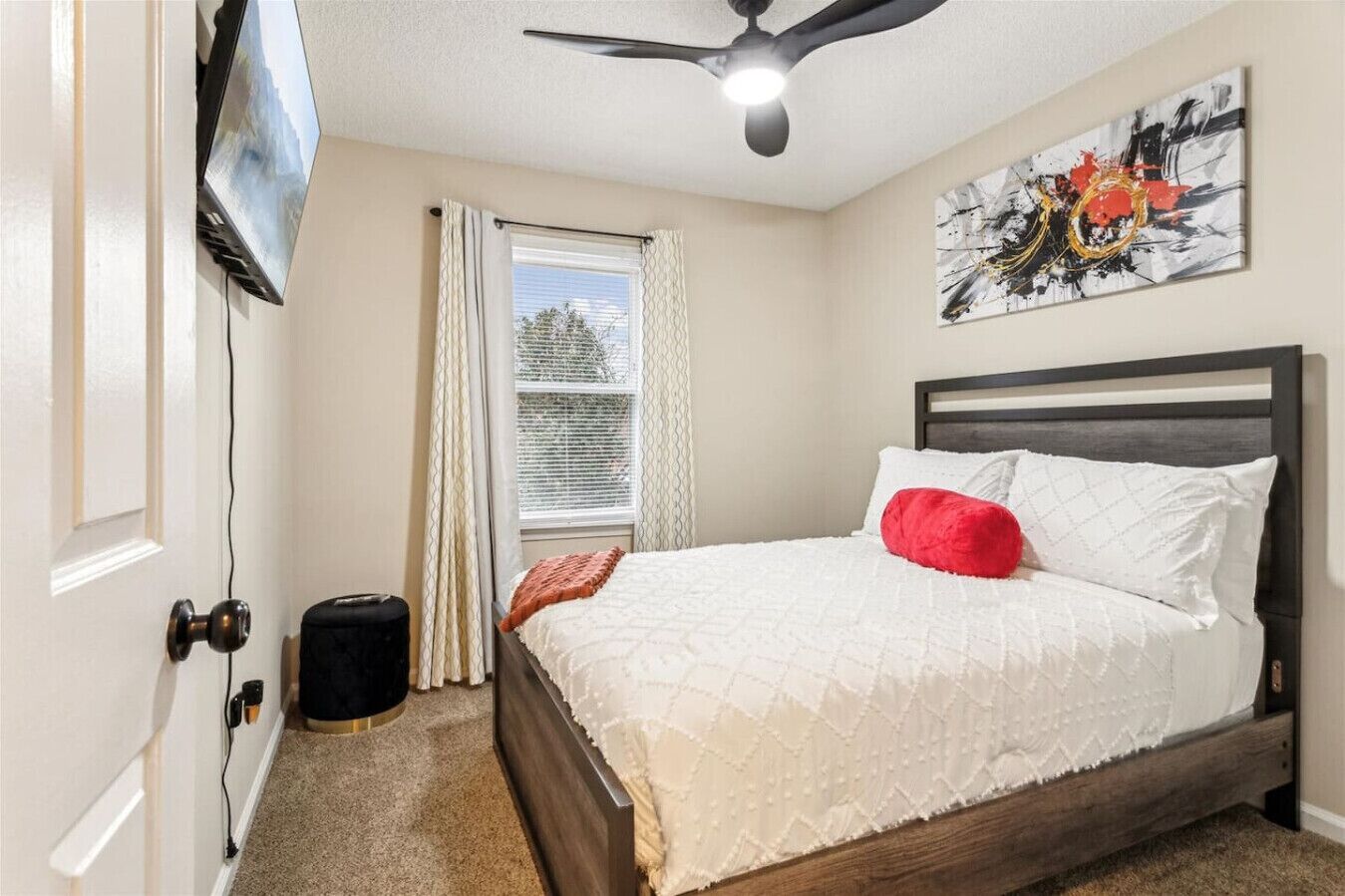 Quarto com cama, ventoinha no teto, janela com cortinas e um quadro na parede.