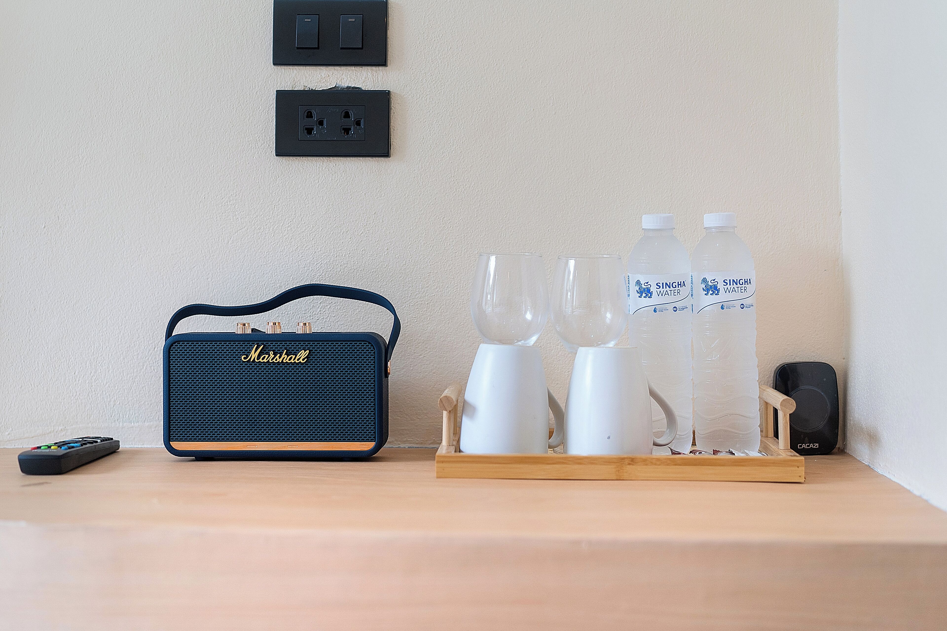 A wooden table with a blue Marshall speaker, two white water bottles, and a remote control.