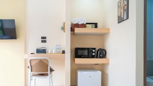 A compact kitchenette with a microwave, coffee maker, and a small refrigerator. There is a chair and a shelf with towels and toiletries. - Amaleena Pool Access, Phuket (Rawai)