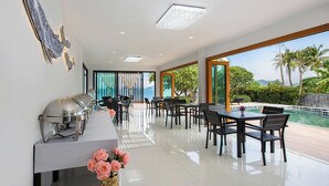 A modern dining area with a buffet setup, large windows with a view of the sea, and a poolside seating area. - Amaleena Pool Access, Phuket (Rawai)