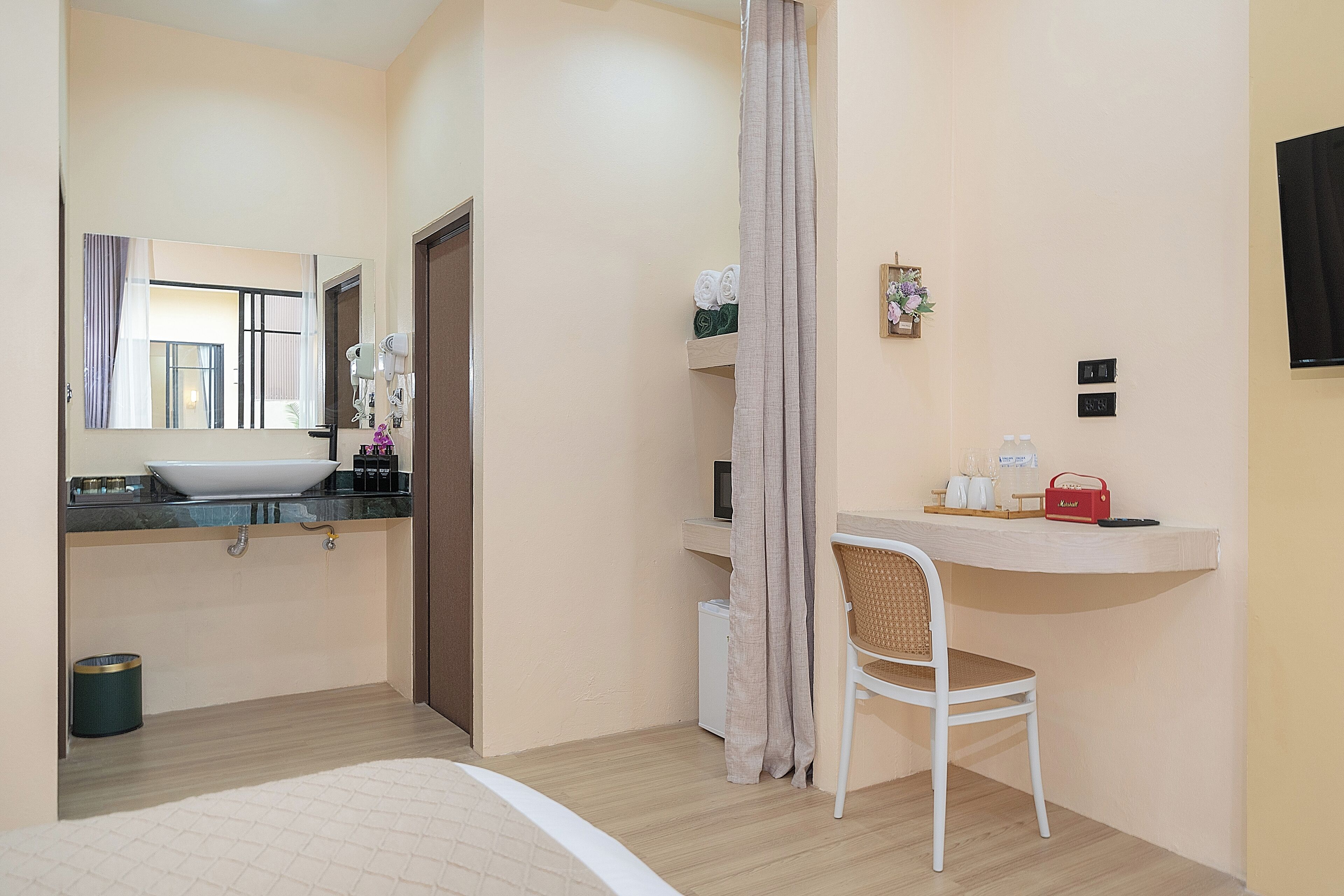 A hotel room with a bed, a bathroom with a sink and mirror, a chair, a small table with toiletries, and a TV mounted on the wall.