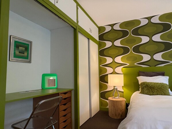 Habitación de hotel con escritorio, silla, cama y una pared con diseño ondulado.