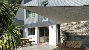 A wooden deck with picnic tables, a stone wall, and a house with a grey roof and white siding. - La Maison de l'Orbière - Suite (Forcé)