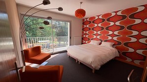 A modern bedroom with a large bed, a sofa, a balcony with a table and chairs, and a patterned wall. - La Maison de l'Orbière - Suite (Forcé)