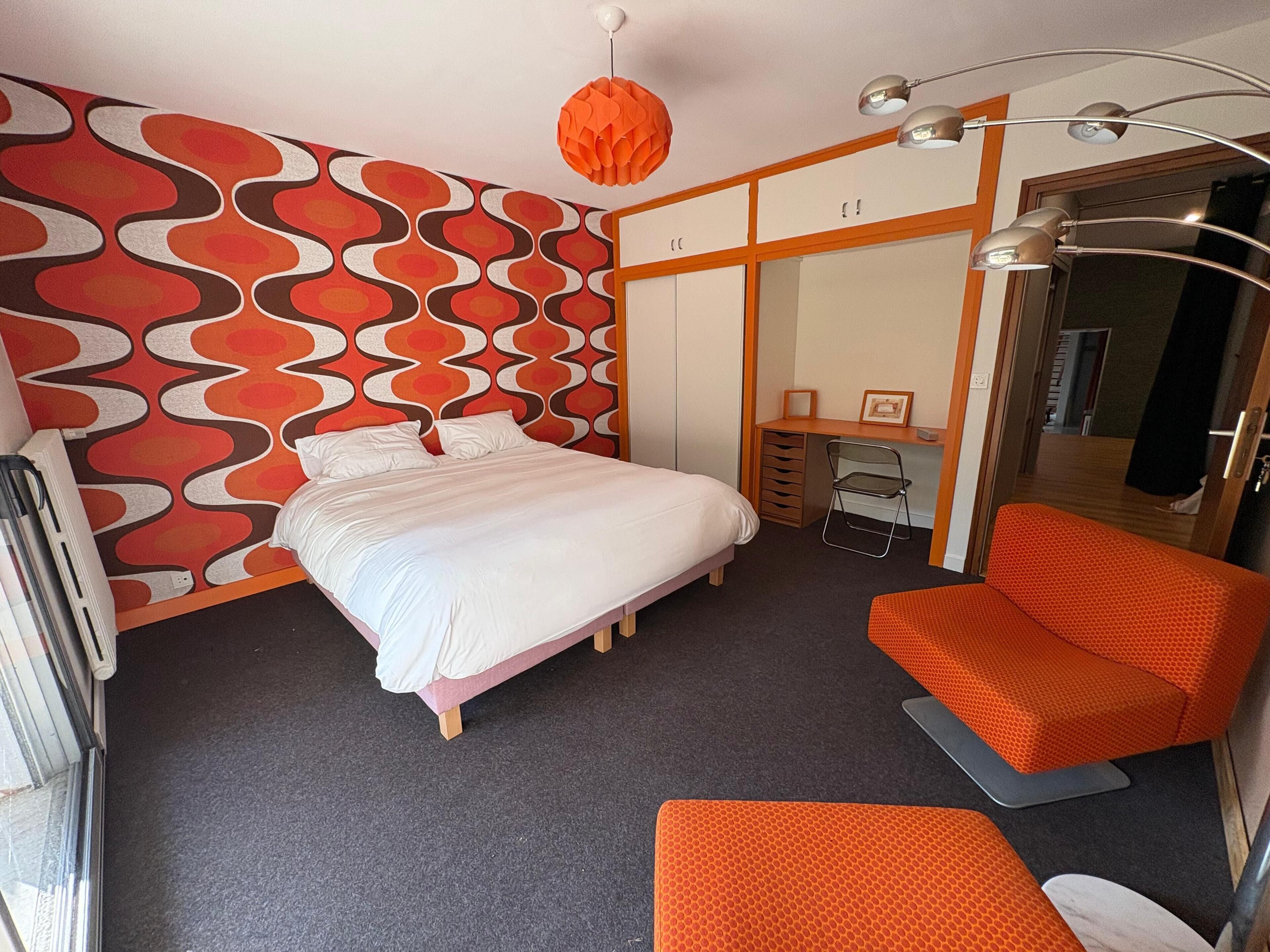 Quarto de hotel com cama, escrivaninha, cadeira e guarda-roupa.