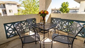 Een balkon met een tafel en stoelen, een vaas met bloemen en uitzicht op gebouwen en bomen.