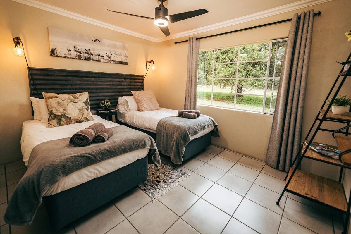 Ein Schlafzimmer mit zwei Betten, einem Deckenventilator, einem Fenster mit Vorhängen und einem Bücherregal.