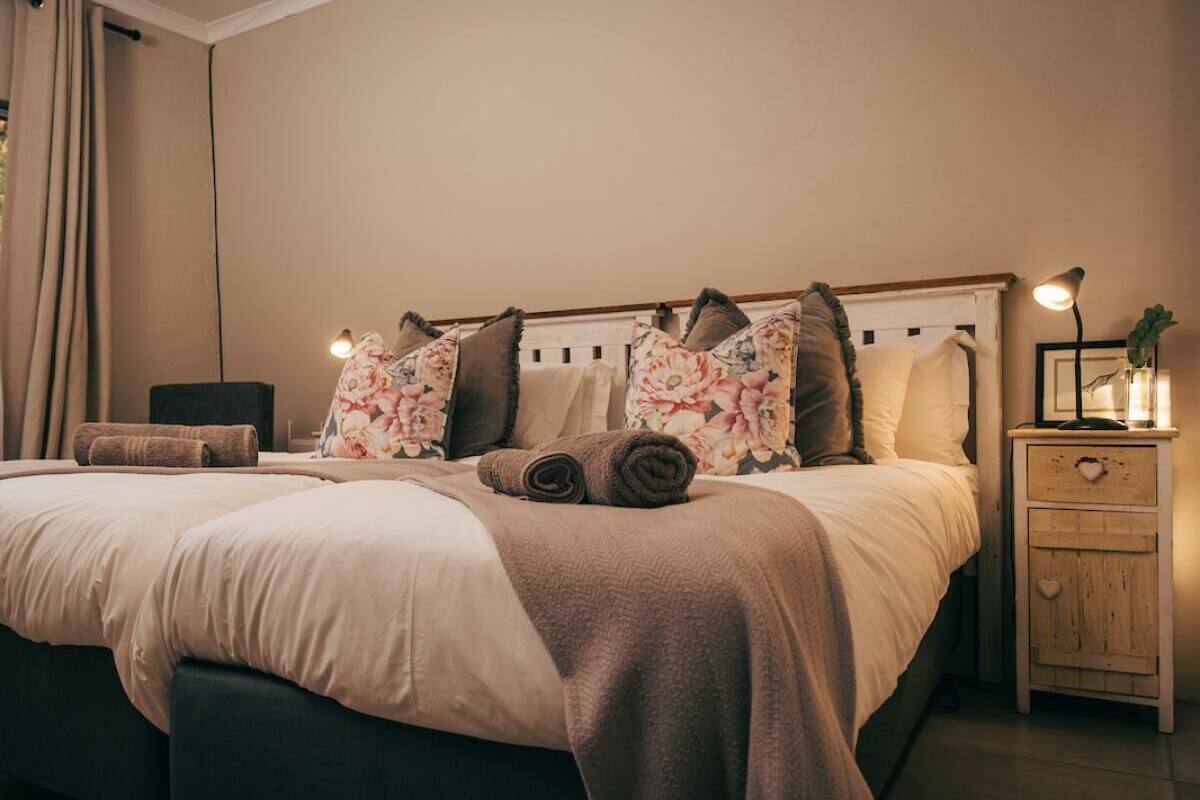 Ein ordentlich bezogenes Bett mit floralen Kissen, einer Nachttischlampe und einem kleinen Holfnachtkästchen.