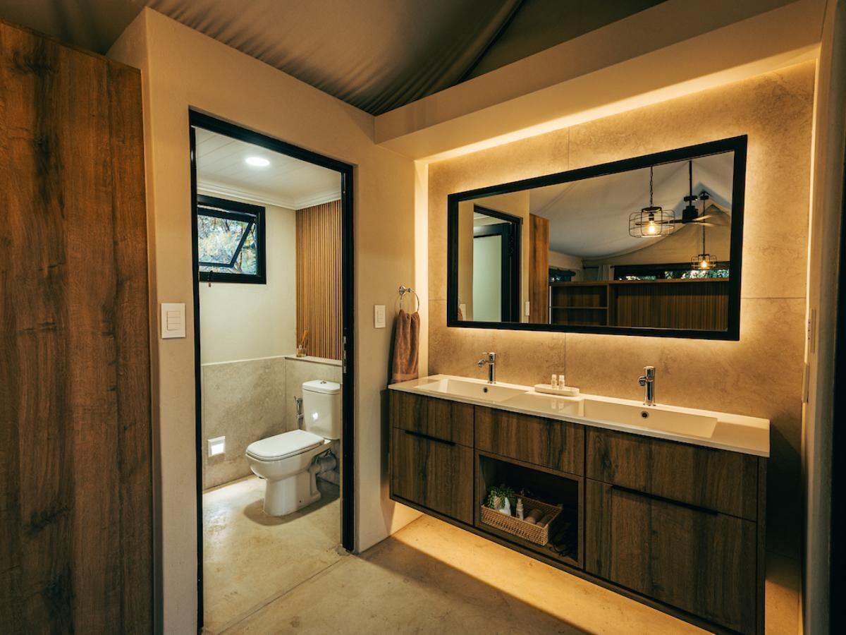 A modern bathroom with a wooden vanity, a large mirror, and a toilet visible through an open door.