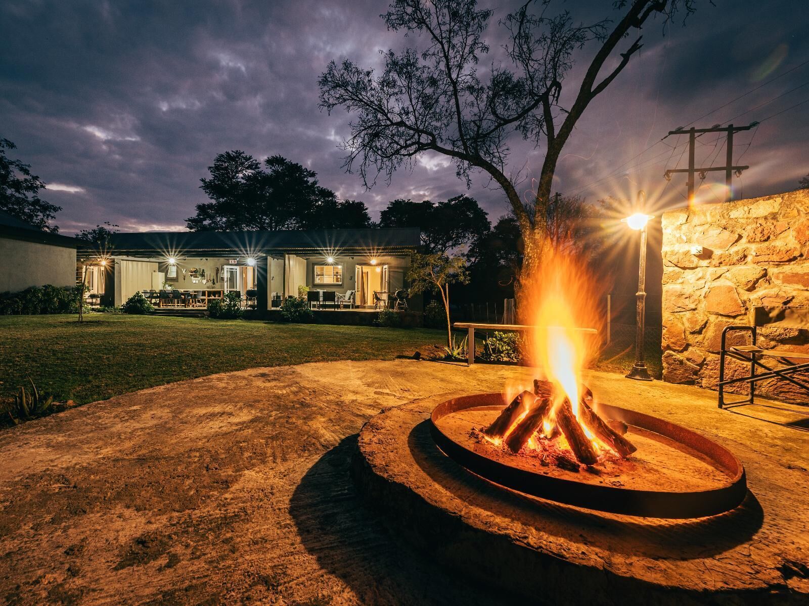 A fire pit in a circular stone basin with a stone wall and a metal railing in the background.