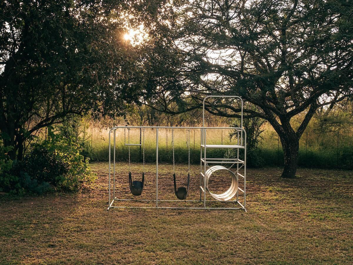 A metal swing set in a grassy area with trees in the background.