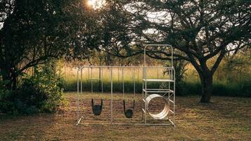 A metal swing set in a grassy area with trees in the background.