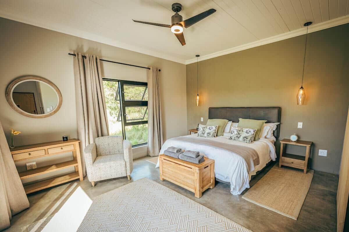 Ein Schlafzimmer mit einem Bett, Nachttischen, einem Sessel, einem Spiegel und einem Deckenventilator.