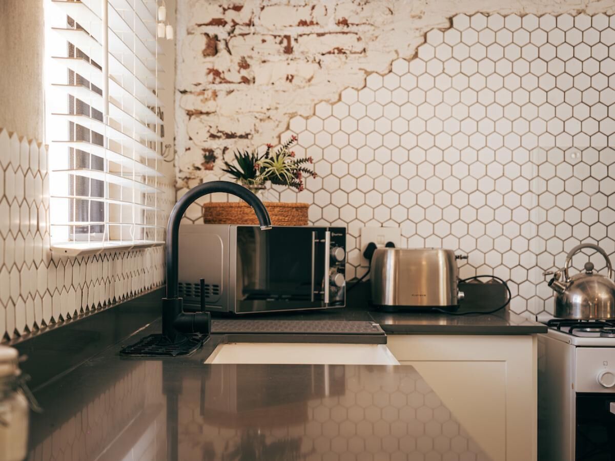 A kitchen with a microwave, toaster, kettle, and a window with blinds.