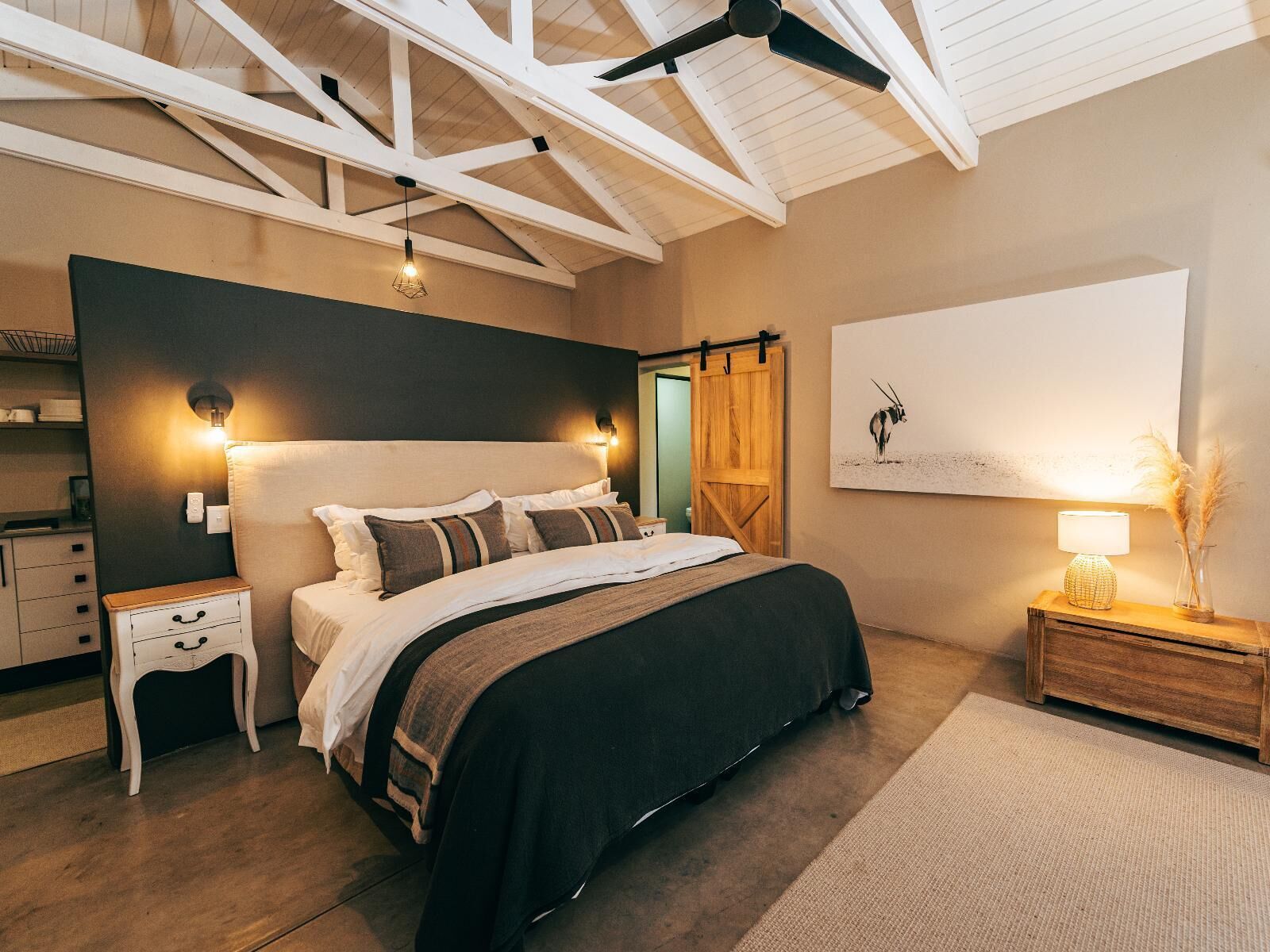 A bedroom with a large bed, a wooden headboard, a ceiling fan, and a wall-mounted lamp.