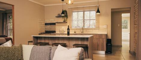A modern kitchen with a central island, bar stools, pendant lighting, and a view to the dining area.
