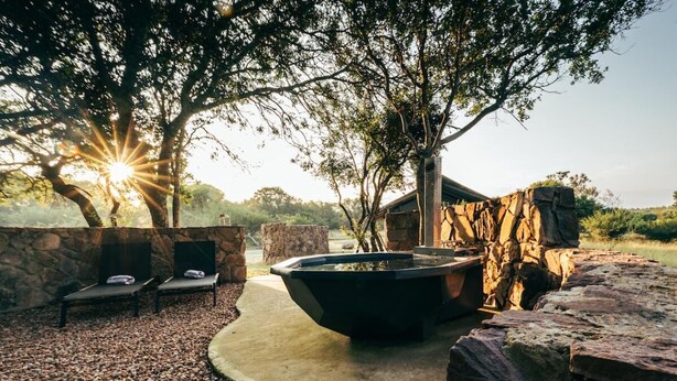 An outdoor seating area with stone walls, a fire pit, and lounge chairs. - Summerplace Game Reserve (Vaalwater)