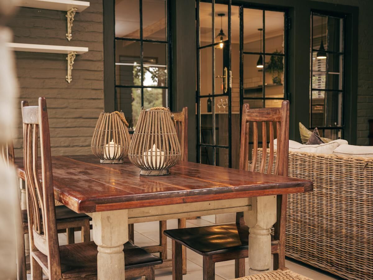 A wooden dining table with two candle holders, surrounded by wicker chairs and a wicker sofa.