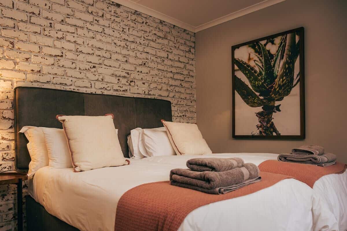 Ein Hotelzimmer mit Ziegelmuster-Wand, einem großen Bett mit weißer Bettwäsche und einer gerahmten Pflanze an der Wand.