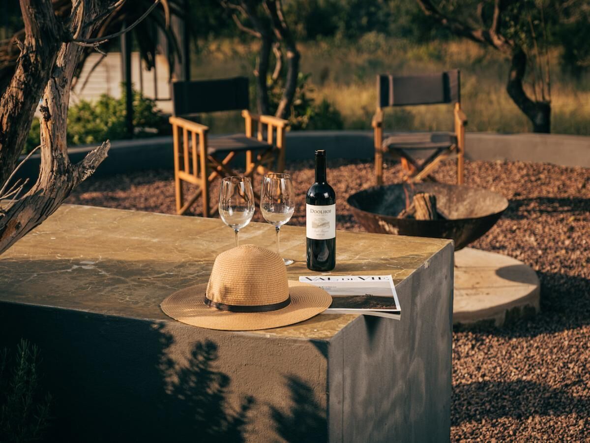 Uma mesa de madeira com uma garrafa de vinho, duas taças e um chapéu de palha.