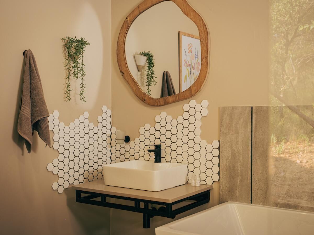 A bathroom with a hexagonal tile wall, a white sink, a black faucet, a wooden-framed mirror, and a towel hanging on the wall.
