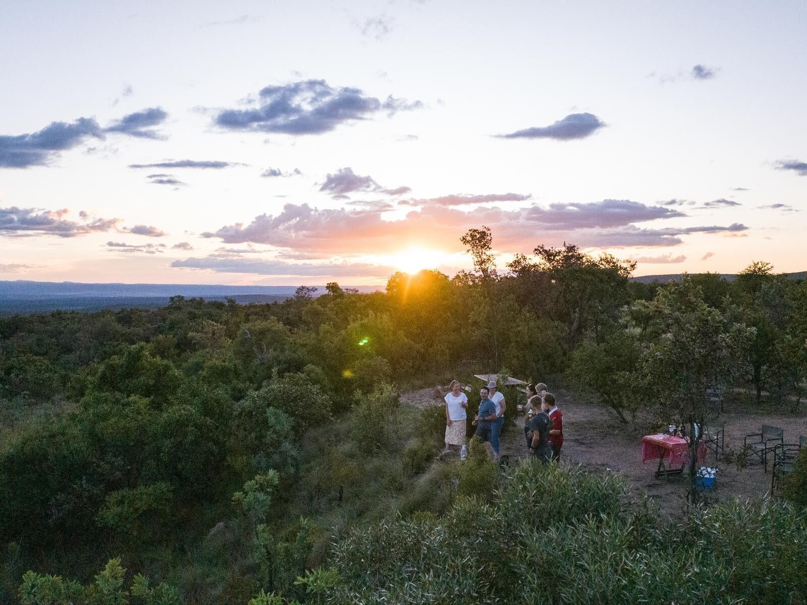 Eine Gruppe von Menschen versammelt sich draußen bei Sonnenuntergang an einem Tisch mit Stühlen.