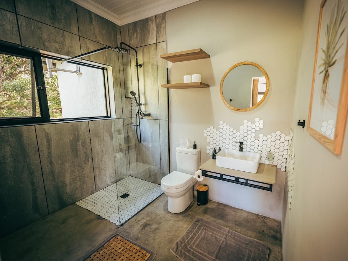 A bathroom with a glass-enclosed shower, a toilet, a sink with a honeycomb tile backsplash, and a round mirror.