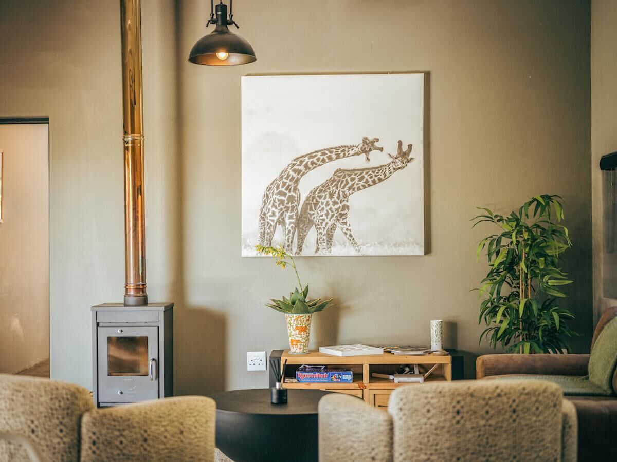 Un salon avec un poêle à bois, une œuvre d’art sur le thème des girafes, une plante en pot et un canapé.