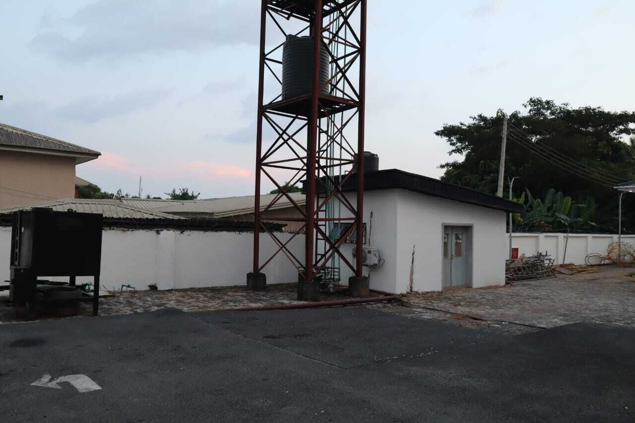 A building with a metal tower structure, a small attached building, and a paved area.