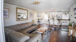 A modern living room with a sectional sofa, a coffee table, and a dining area with a white table and chairs. - Xlnc Exotic Home Sunnyside by sdstay (San Diego)