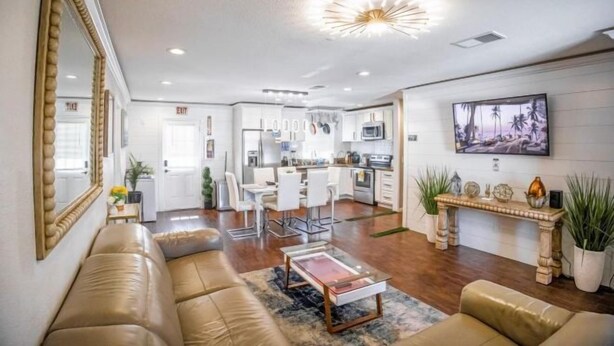 A spacious living area with a sofa, coffee table, and a dining area with chairs. There is a kitchen in the background with modern appliances and a large TV mounted on the wall. - Xlnc Exotic Home Sunnyside by sdstay (San Diego)