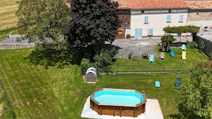 Un jardin avec une piscine en bois, un petit abri de jardin et un espace clôturé comprenant des chaises d’extérieur.
