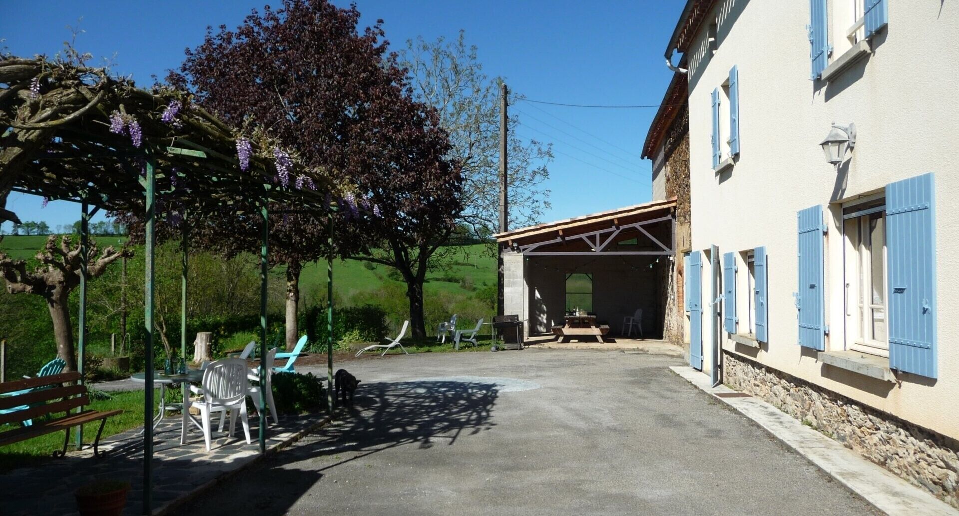 Un bâtiment doté d’un espace extérieur abrité, d’un banc et d’un arbre aux fleurs violettes.