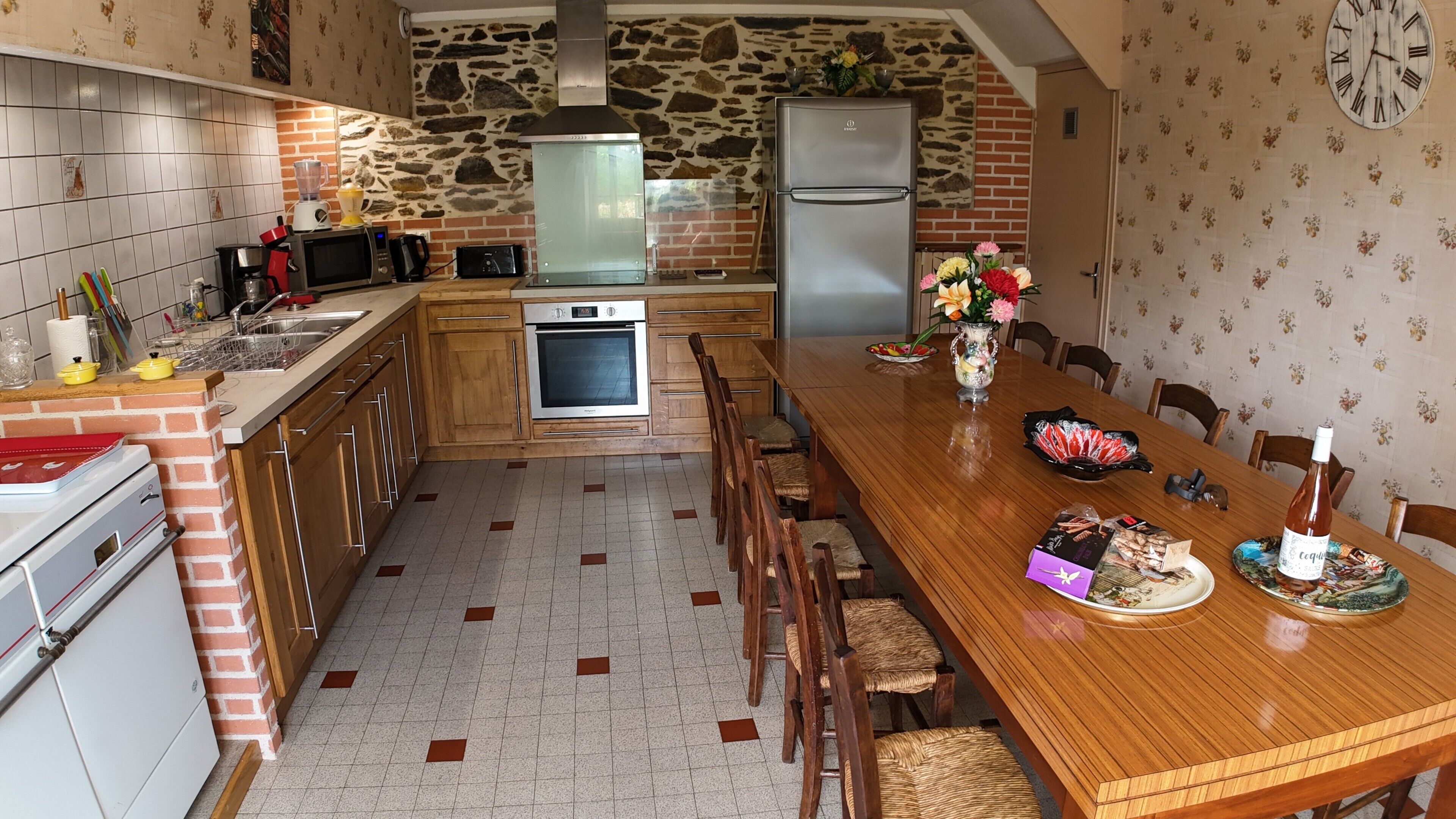 Una cocina con pared de ladrillo, pared de piedra, mesa de comedor de madera y refrigerador.
