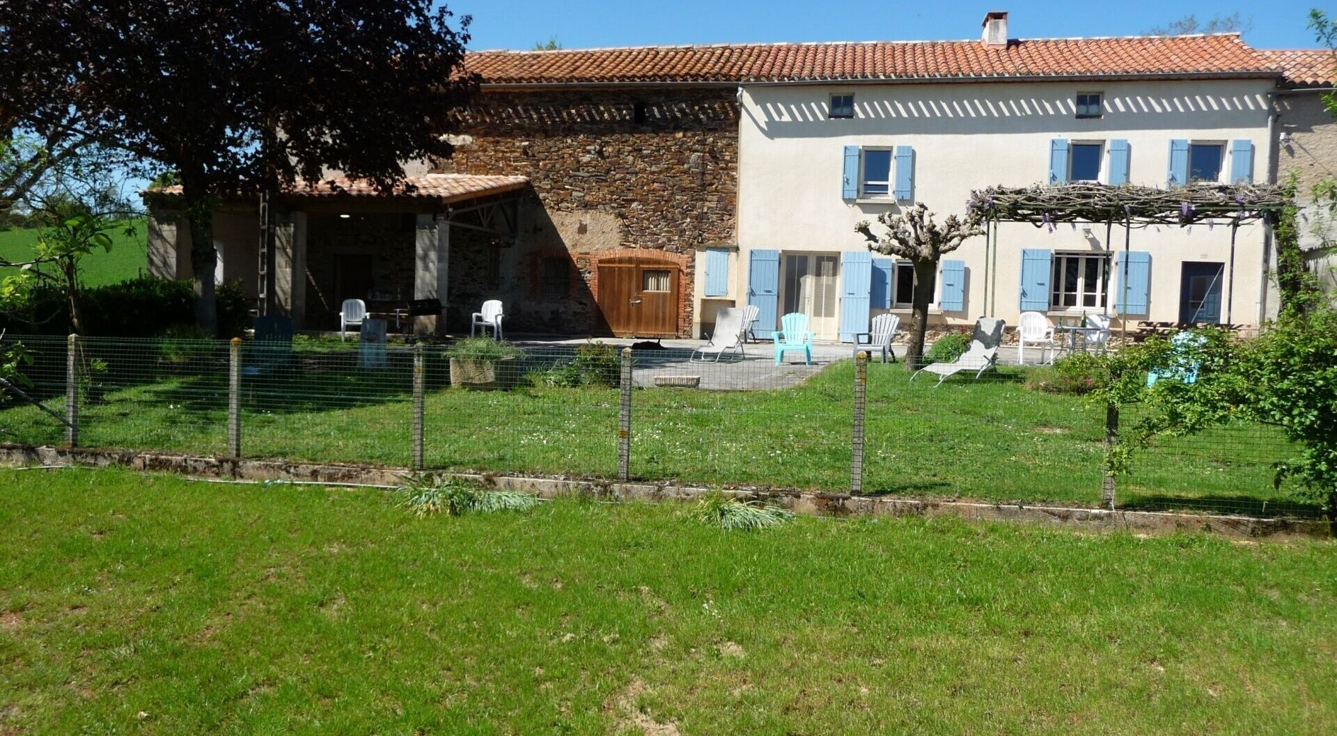 Una casa de dos pisos con fachada de piedra, una puerta de madera y un balcón con sillas blancas.