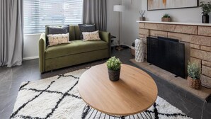Ein modernes Wohnzimmer mit einem grünen Sofa, einem runden Holztisch, einem Kamin und einem großen abstrakten Gemälde an der Wand.