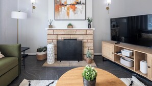 Ein modernes Wohnzimmer mit Kamin, einem grünen Sofa, einem Holztisch mit Pflanze und einem Flachbildfernseher.