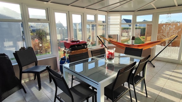 Une véranda avec une table en verre, des chaises, un hamac et un barbecue.