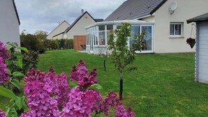 Un quartier résidentiel avec des maisons, une pelouse et des fleurs violettes au premier plan.