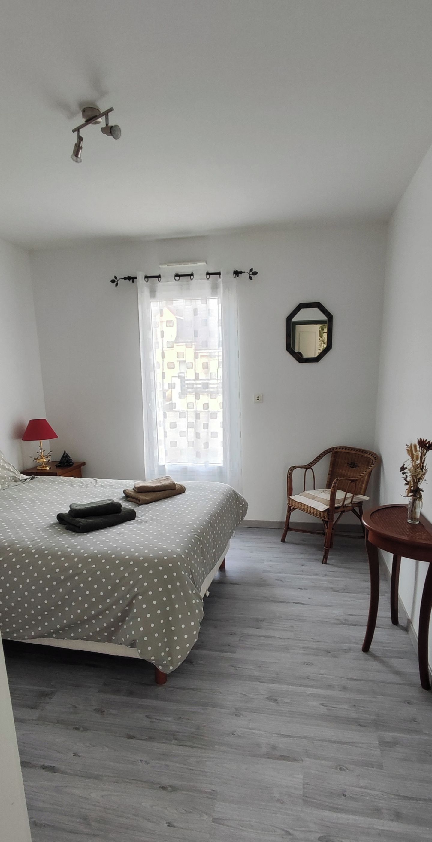 Een slaapkamer met een bed, een stoel, een tafeltje en een raam met gordijnen.