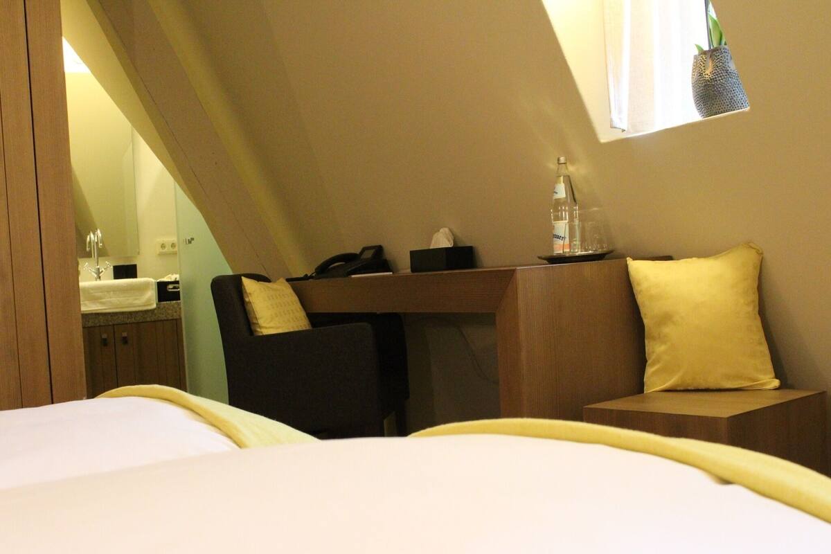A hotel room with a bed, a desk, a chair, and a small table with a pillow.