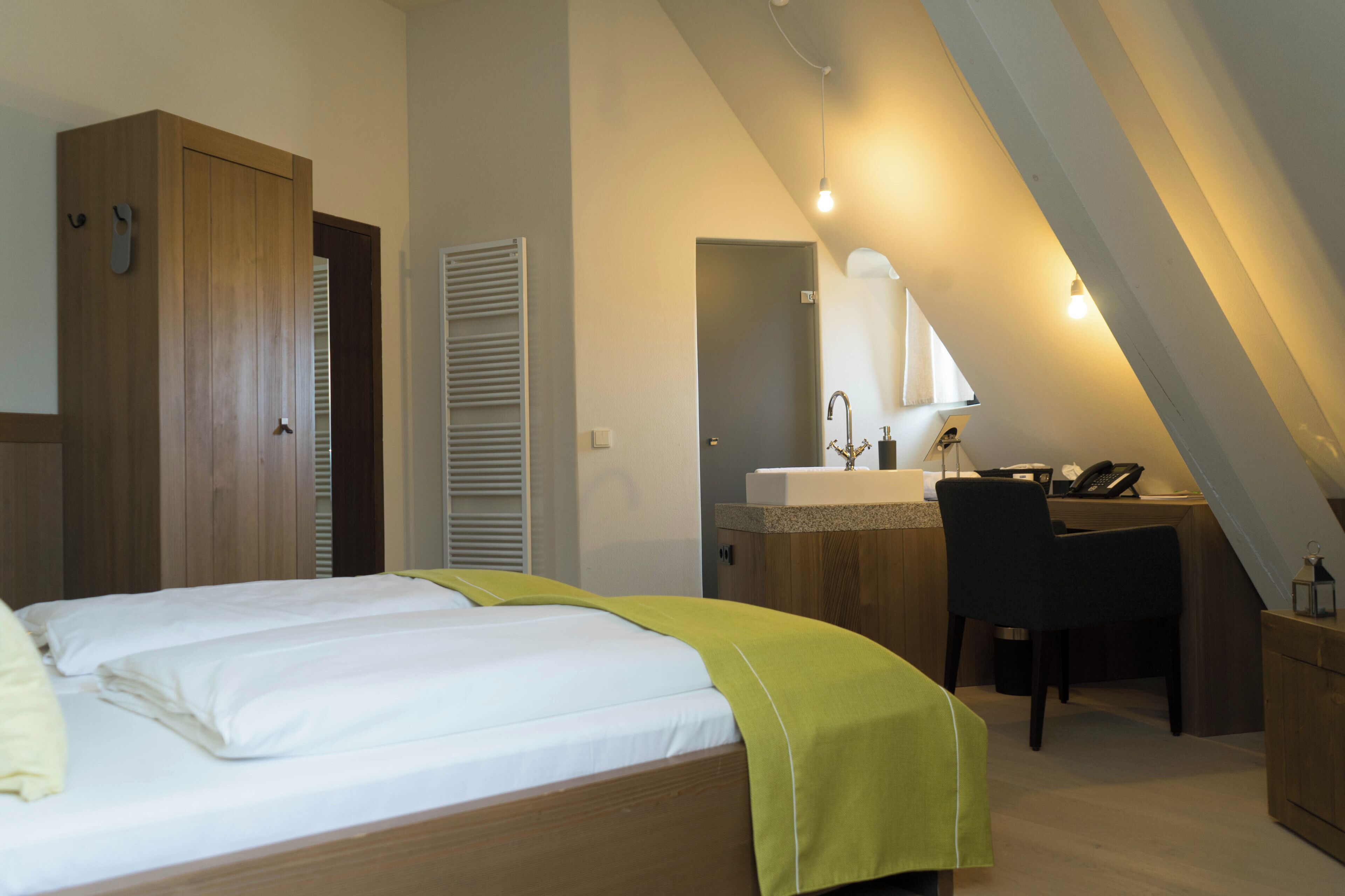 Una camera da letto con un letto, una scrivania, una sedia e un bagno con lavandino e specchio.