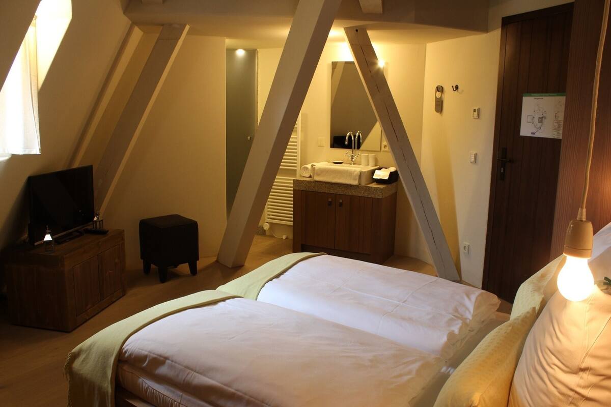 A bedroom with a bed, a television, a small table, and a bathroom with a sink and mirror.