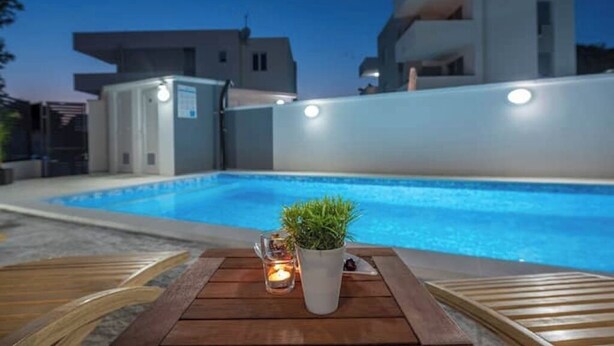 Un espace aménagé au bord de la piscine, avec une table en bois, une plante en pot et une bougie.