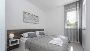 Une chambre moderne avec un grand lit, une table de chevet avec une lampe, une œuvre d’art accrochée au mur et une fenêtre avec des rideaux.