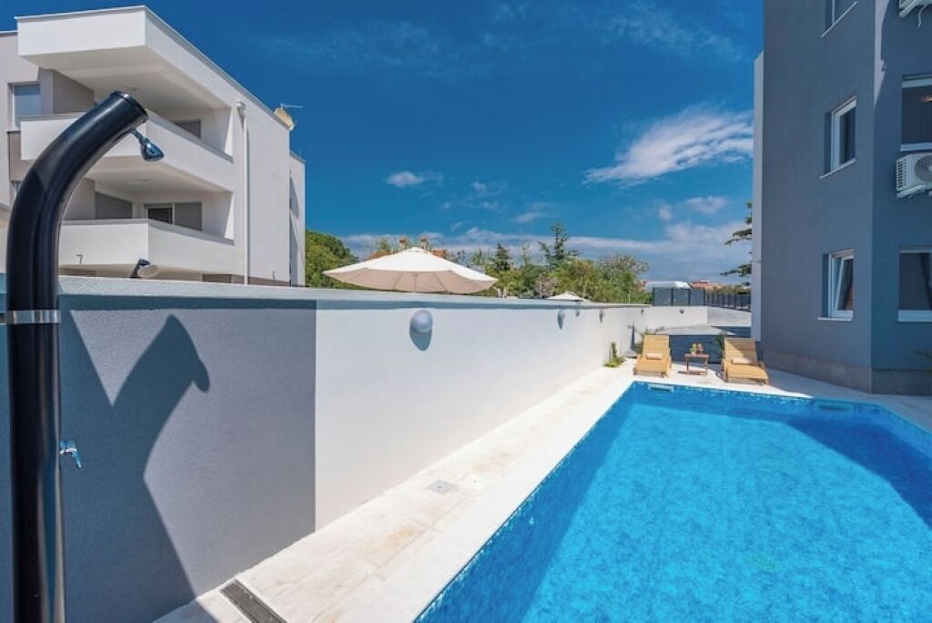 A swimming pool with lounge chairs and umbrellas, surrounded by modern buildings.
