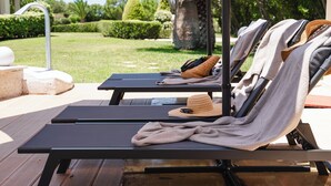 Zona de piscina con sillones de descanso, toallas y un sombrero.