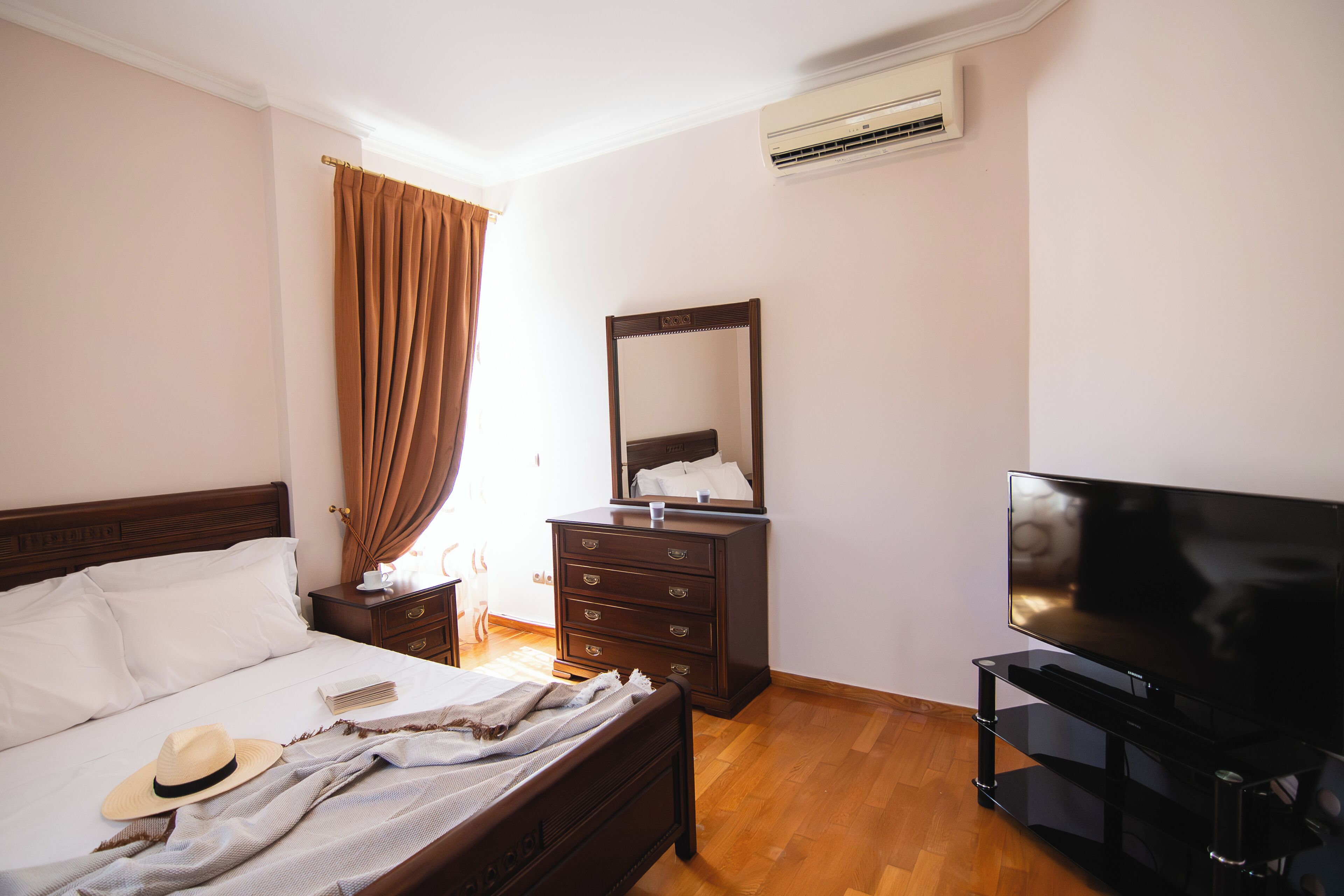 A hotel room with a bed, a dresser, a TV, and an air conditioning unit.
