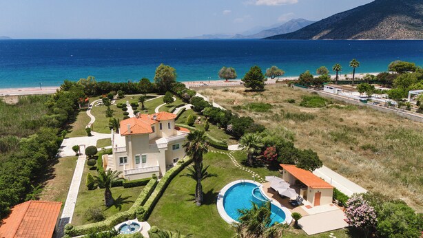 Una casa grande con piscina, rodeada de jardines cuidados y vista al mar.